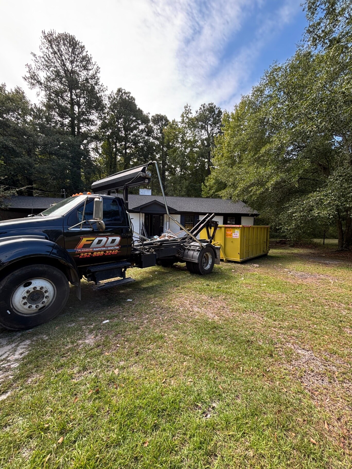 Flashbang roll-off truck hauling the loaded yellow dumpster away from the same house, with the lawn clear