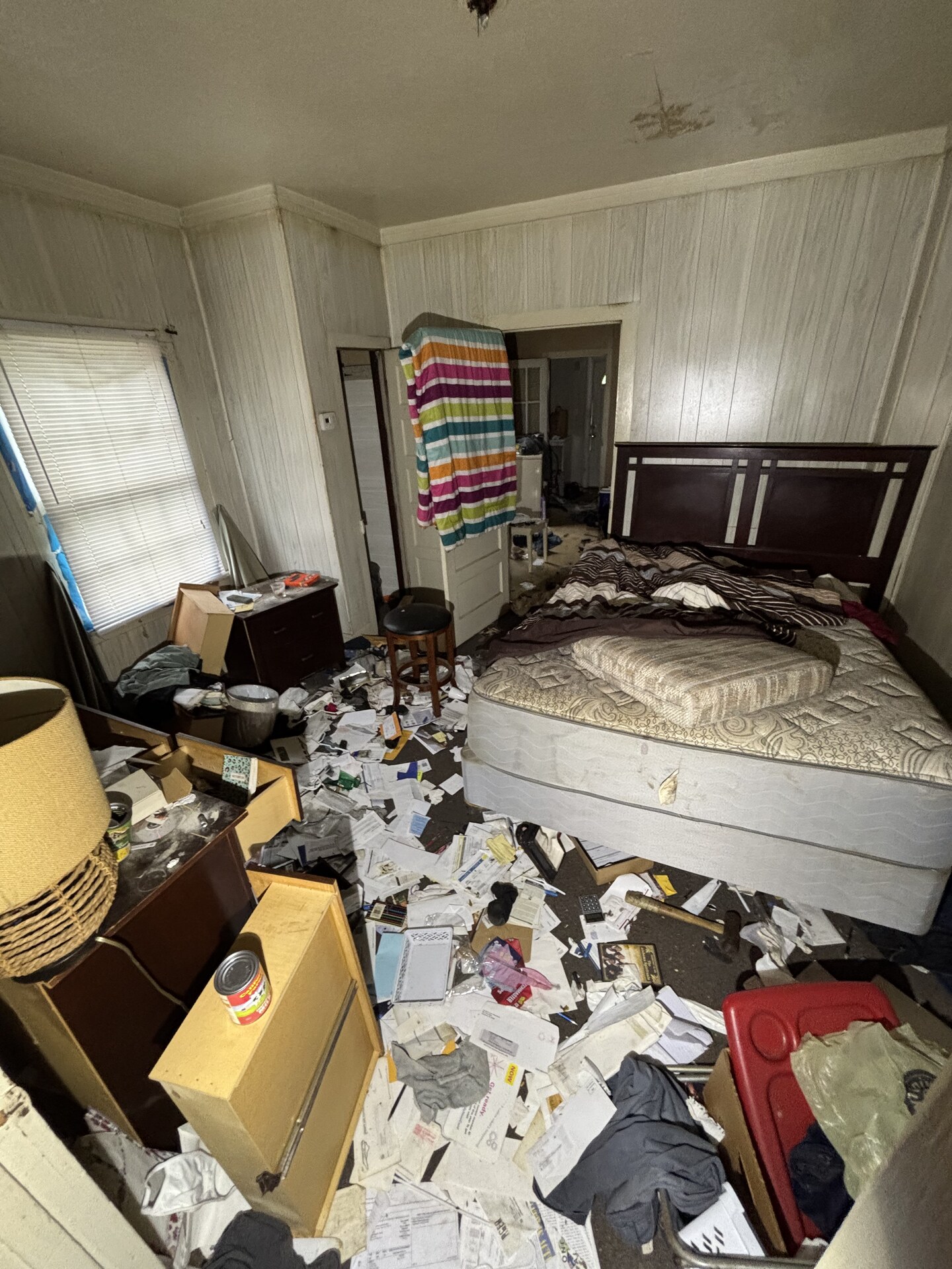 Bedroom stacked with a mattress, furniture, and scattered junk before a house cleanout