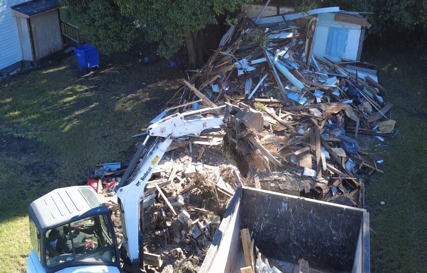 Mini excavator clearing a demolition site beside a roll-off dumpster